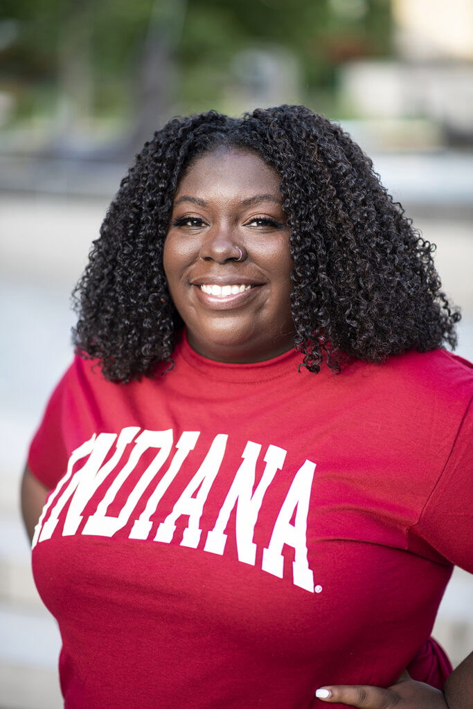 Christen Priddie posing in a red Indiana tshirt with medium length dark brown hair.